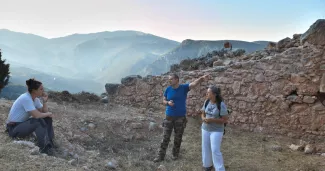 Discussion à l'aube, en juillet 2021, avant le début d'une journée de fouille. Derrière les archéologues, une section des remparts tardifs de Delphes et le paysage matinal des hautes vallées de Phocide. Ministère grec de la culture/Ecole française d'Athènes/Mission fortifications de Delphes/K. Robert


