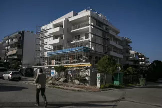 Un homme passe devant un immeuble en construction dans la banlieue sud d’Athènes, le 30 mars 2024.  ARIS MESSINIS / AFP  