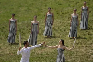 L’actrice Mary Mina, qui interprête la « grande prétresse » , tend un rameau d’olivier au premier porteur de la flamme olympique, le Grec Stefanos Ntouskos, le 16 avril 2024, à Olympie (Grèce).  PETROS GIANNAKOURIS / AP  